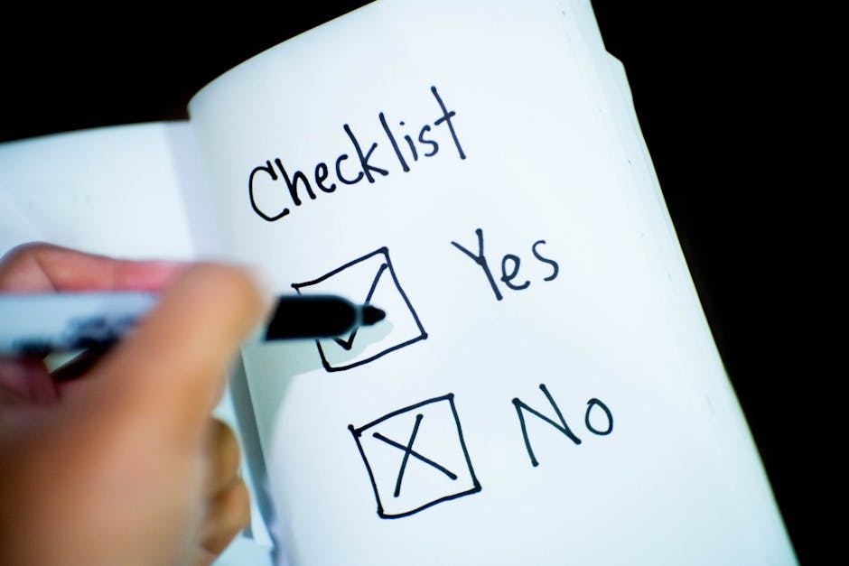 A person is holding a black marker and checking off a box labeled 'Yes' on a white paper sheet titled 'Checklist'. The checklist has two options: 'Yes' with a checked box and 'No' with an unchecked box. The paper is held in one hand and appears to be part of a larger document or notepad. The background is dark and out of focus, emphasizing the checklist and the hand. This image represents the process of planning or confirming tasks related to house removals or moving logistics, with an emphasis on thorough packing, organization, and checklist completion often involved in furniture transport and home relocation services offered by companies like Man and Van Harlington.