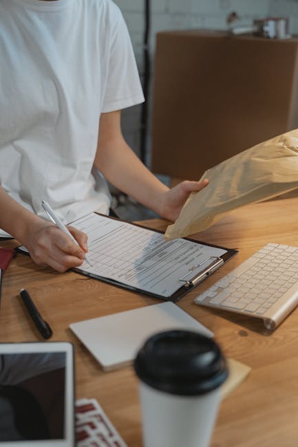 Close-up image of a person’s hand holding a black marker and writing a house removal checklist in a grid notebook. The checklist includes items such as 'check list,' 'arrival,' 'pack,' and 'loading.' The person is inside a property, with a glimpse of a black storage box and some yellow objects, possibly furniture or household items, visible in the blurred background. The scene captures the preparation and organisation process involved in home relocation, with a focus on packing, loading, and logistical steps. The lighting is natural, highlighting the careful documentation necessary for a smooth moving and furniture transport process. Man and Van Harlington, a company specialising in removals, often assist clients with packing and moving logistics, as reflected by the detailed planning shown in this image.